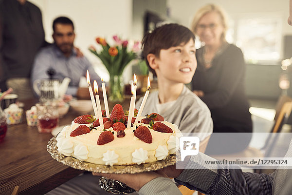 Close-up of grandfather holding birthday cake with family in background