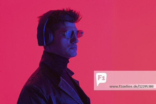 Young male fashion model wearing headphones and sunglasses against coral background