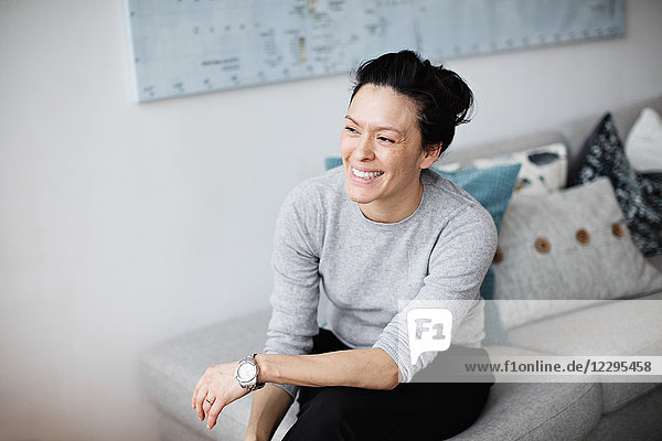 Smiling mid adult woman looking away while sitting on sofa at home