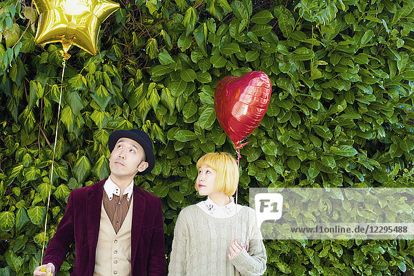 Couple looking at balloon while standing against plants