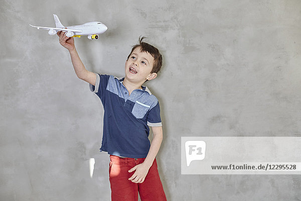 Junge spielt mit dem Modellflugzeug und steht an der grauen Wand