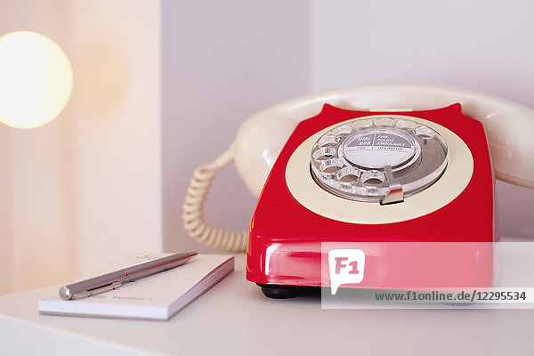 Nahaufnahme des roten Telefons mit Tagebuch und Stift auf dem Tisch zu Hause
