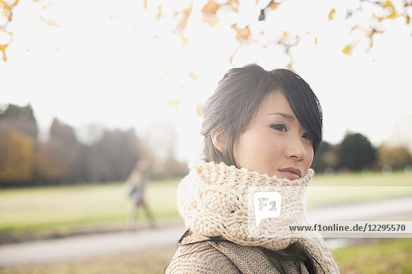 Nahaufnahme einer nachdenklichen jungen Frau mit Schal und Blick in den Park