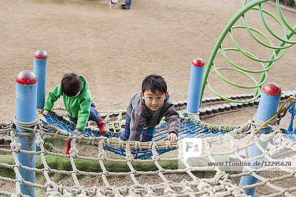 Hochwinkelansicht der Jungen beim Klettern am Netz auf dem Spielplatz