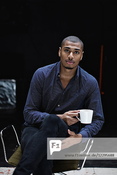 Portrait of young businessman having coffee while sitting on chair at office