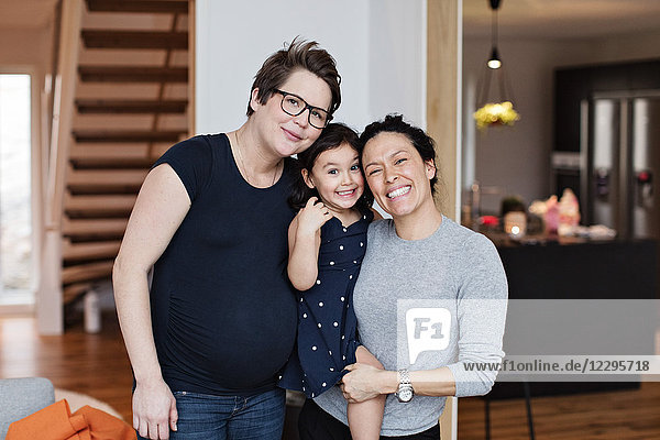 Portrait of smiling lesbian couple with daughter in living room at home