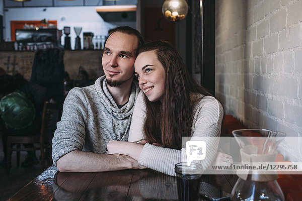 Happy young couple looking away while sitting at cafe