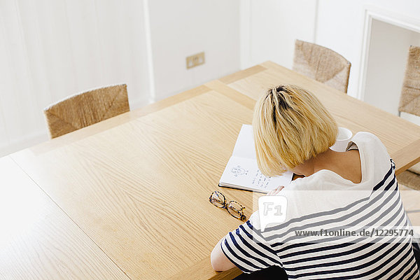 High angle view of woman with short hair writing in diary at table