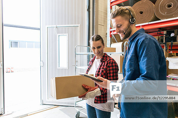 Smiling man showing digital tablet to female coworker holding box in distribution warehouse