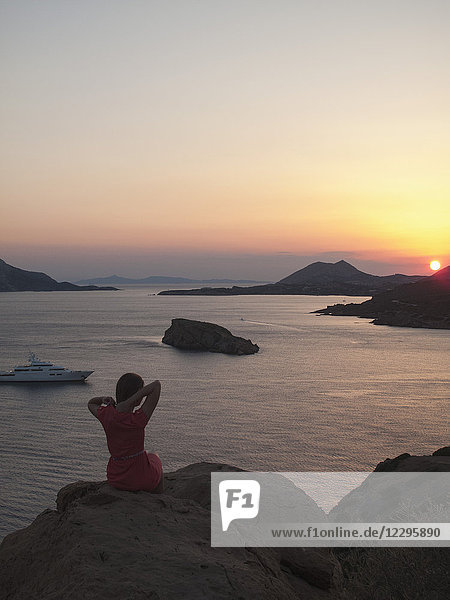 Rückansicht einer Frau  die auf einer Felsformation sitzt und den Sonnenuntergang über dem Meer gegen den Himmel betrachtet  Griechenland