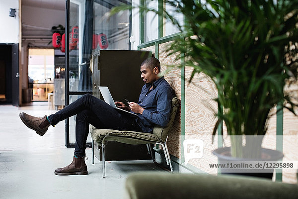 Young businessman using laptop while sitting on chair at creative office