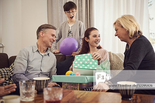 Boy looking at happy sister receiving gifts from grandparents at home