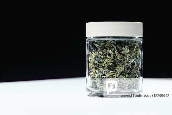 Marihuana-Blätter im geschlossenen Glas auf Tisch vor schwarzem Hintergrund