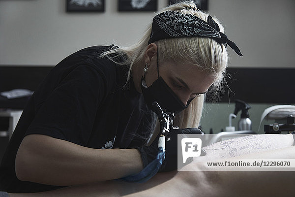 Künstlerin mit Masken-Tätowierung auf dem Oberschenkel der Frau im Atelier