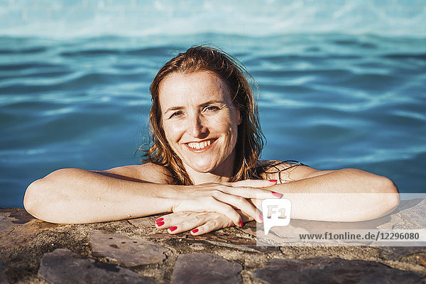 Porträt einer glücklichen Frau am Pool an einem sonnigen Tag