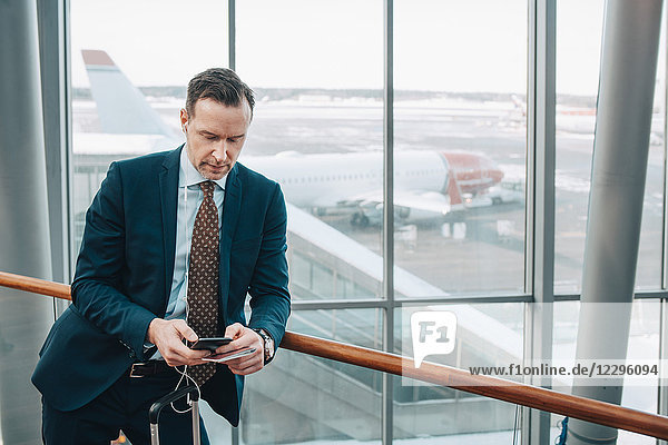 Businessman using mobile phone while leaning on railing in airport