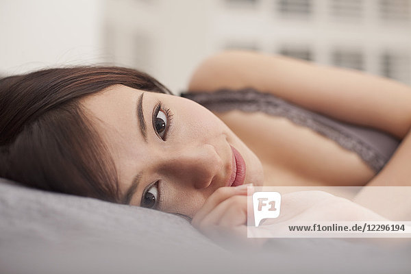 Close-up portrait of beautiful woman lying on bed at home
