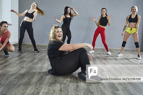 Lachende Frau sitzt auf dem Boden  während sie mit Freunden im Studio tanzt.