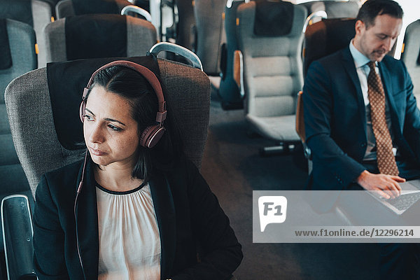 Businesswoman using headphones while traveling with businessman in train