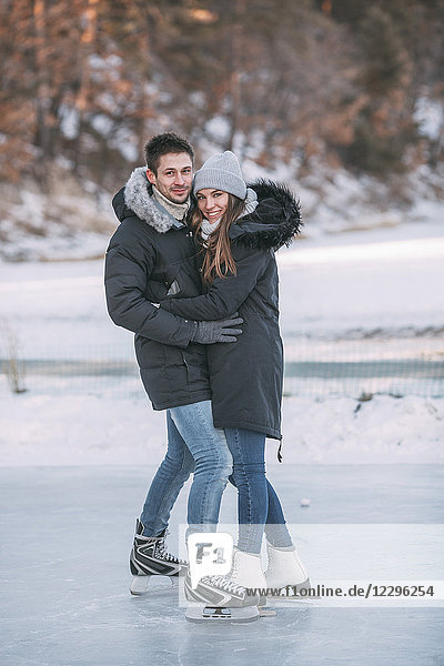 Portrait eines glücklichen Paares  das sich beim Eislaufen auf der Eisbahn umarmt.