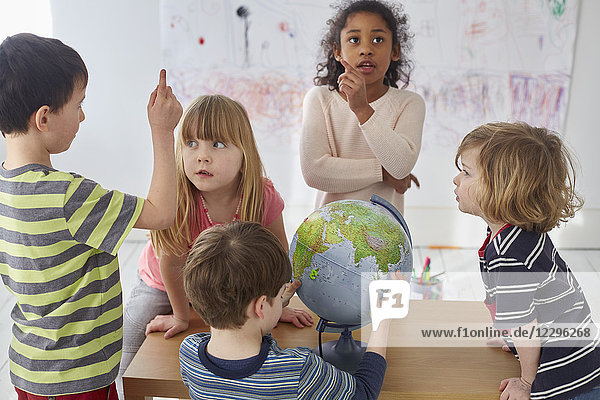 Kinder diskutieren bei der Erkundung des Globus bei Tisch in der Vorschule