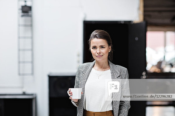 Portrait of beautiful smiling businesswoman having coffee while standing at office
