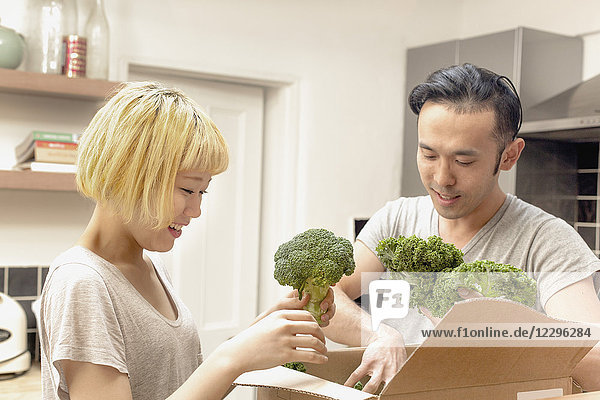 Lächelndes junges Paar  das frisches Gemüse aus dem Karton nimmt.