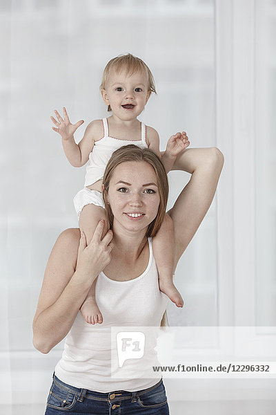 Porträt einer glücklichen Mutter  die ihre Tochter auf den Schultern trägt.