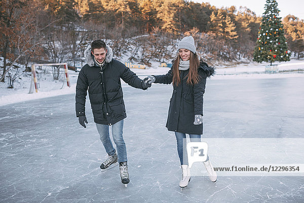 Volle Länge des glücklichen Paares beim Eislaufen auf der Eisbahn und Händchenhalten