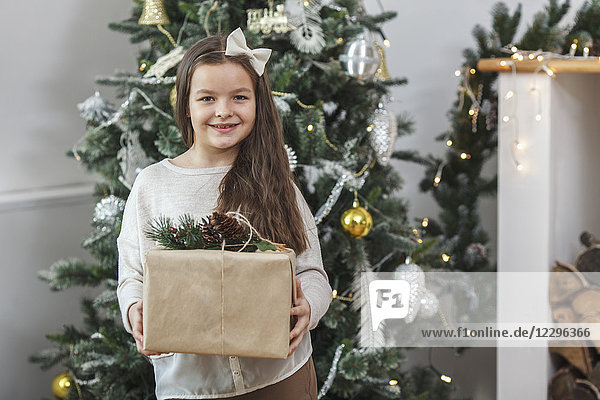 Portrait of smiling girl holding gift against Christmas tree at home