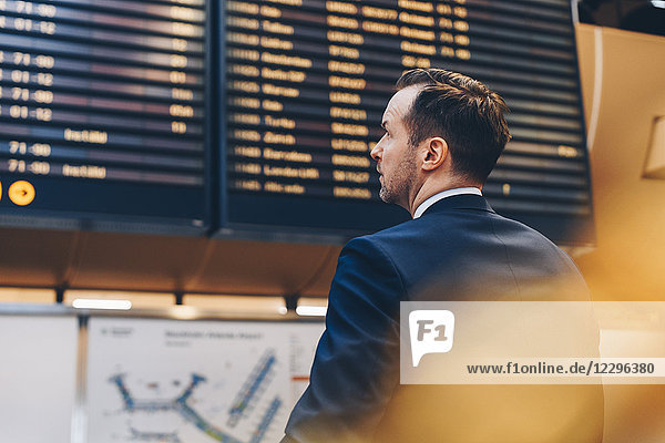 Rear view of businessman looking at arrival departure board in airport
