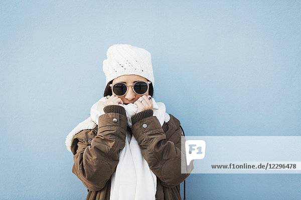 Fashionable woman wearing warm clothing standing against blue background