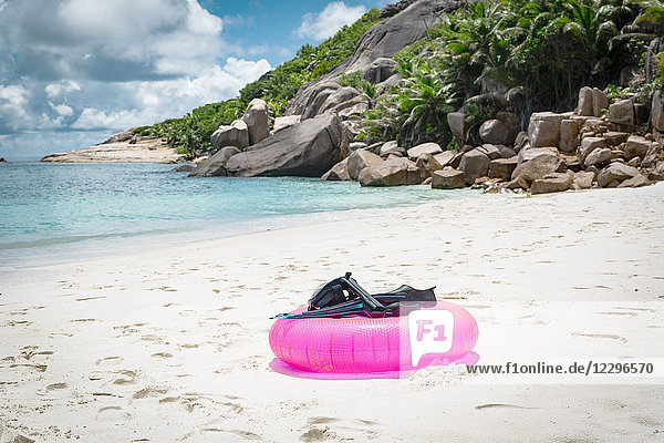 Tauchflossen mit Tauchermaske auf rosa aufblasbarem Ring am Strand gegen bewölkten Himmel  Seychellen