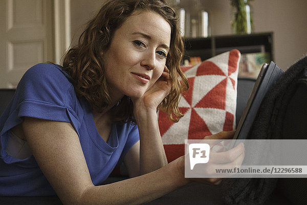 Portrait of confident woman using digital tablet on sofa at home