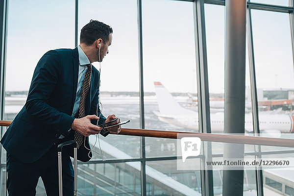 Businessman looking at airplane through window while using mobile phone in airport