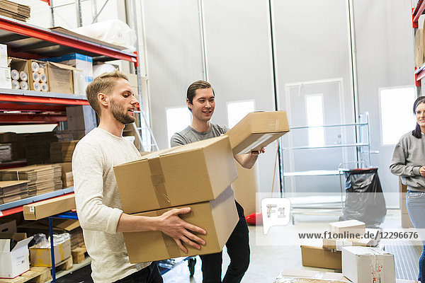 Woman looking at coworkers carrying boxes in distribution warehouse