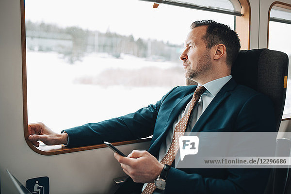 Thoughtful businessman holding mobile phone while traveling in train