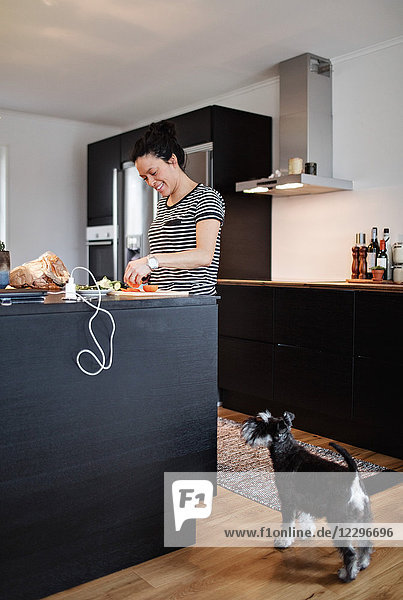 Dog standing by smiling woman cooking food at kitchen