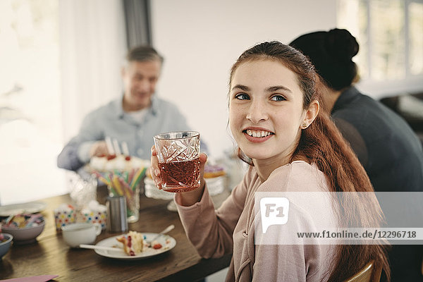 Smiling girl having drink while sitting with family at table during party