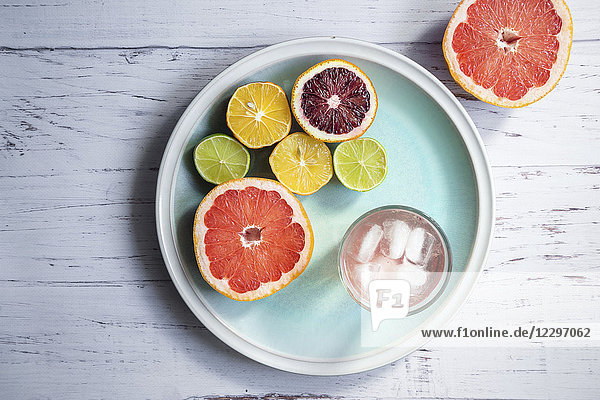 Halbierte Zitrusfrüchte  ein Glas Grapefruit-Wasser mit Eis auf einem blauen Teller