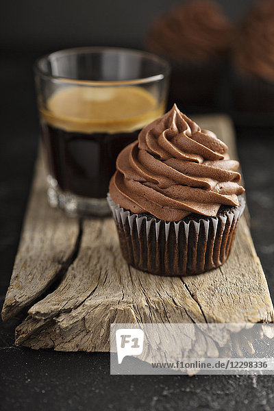Dunkle Schokolade Cupcakes mit Ganache-Glasur auf dunklem Hintergrund mit Espresso in einem Glas