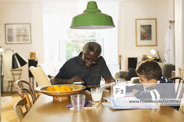 Grandfather at dining table with grandson doing homework