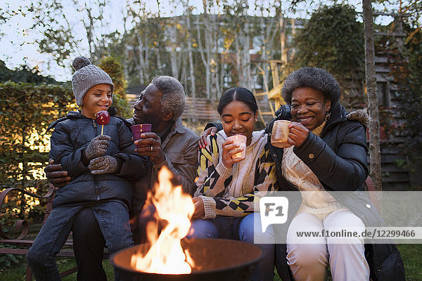 Grandparents and grandchildren drinking hot cocoa at campfire