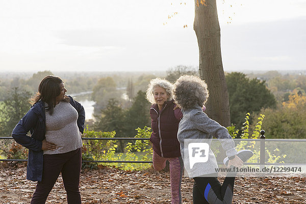 Active senior women friends stretching legs  preparing for run in autumn park