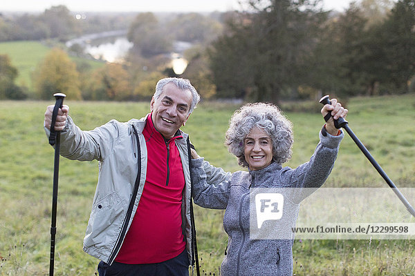 Portrait enthusiastic  confident active senior couple hiking with poles in rural field