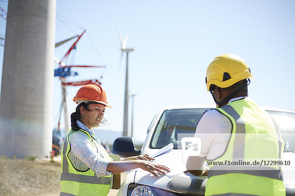 Engineers reviewing blueprints at truck at sunny wind turbine power plant