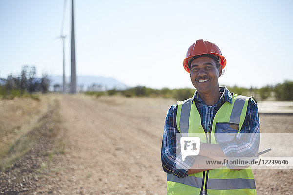 Portrait smiling engineer on dirt road at wind turbine power plant