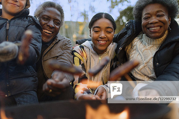 Happy grandparents and grandchildren roasting hot dogs over campfire