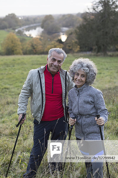 Portrait confident active senior couple hiking with poles in rural field