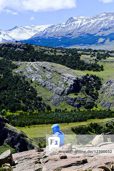 Rear view of hiker in hooded jacket sitting in scenery with mountains  El Chalten  Santa Cruz Province  Patagonia  Argentina
